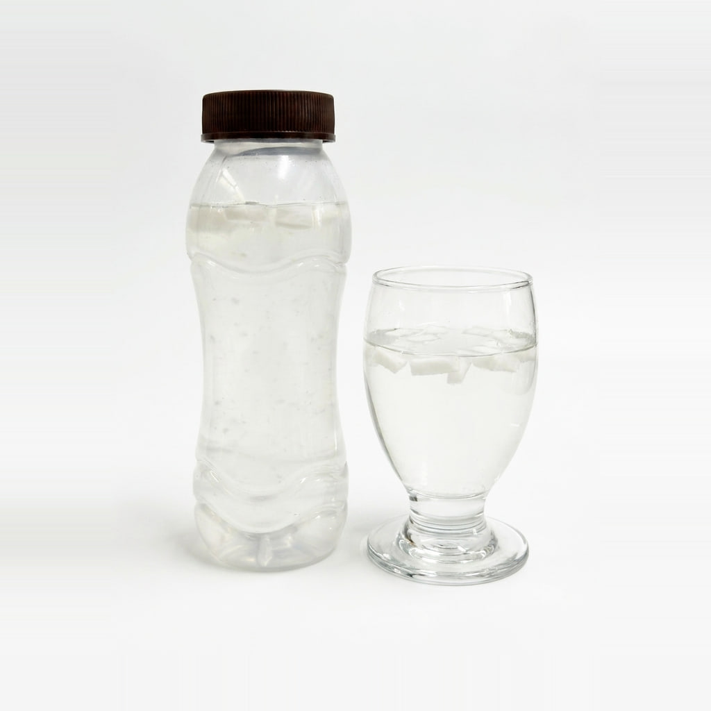 Coconut water with firm coconut chunks, bottle and glass